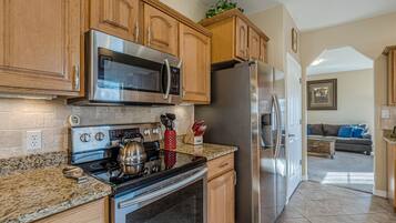 Una cocina con armarios de madera, electrodomésticos de acero inoxidable, encimeras de granito y vistas al área de estar.