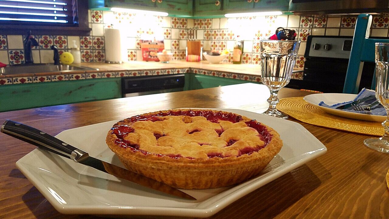 Una torta su un piatto bianco, con un coltello su un tavolo di legno in una cucina con piastrelle colorate.