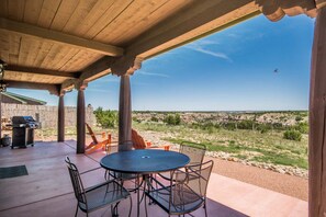 An outdoor patio with a round table and chairs, a grill, and a view of a desert landscape.