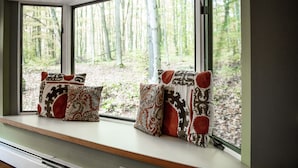 Asiento junto a la ventana con cojines estampados y vistas a un bosque.