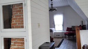 A room with white wooden walls, a brick fireplace, a wooden bench, and a bed with a red blanket.