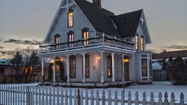 A large, two-story house with a white picket fence, multiple windows, and a chimney.