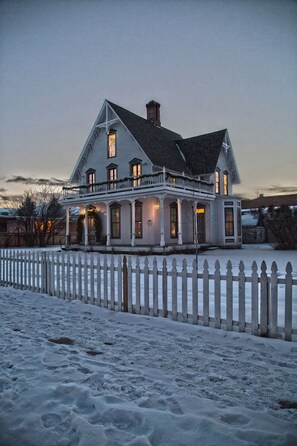 Une grande maison à deux étages, avec une clôture blanche en piquets, de nombreuses fenêtres et une cheminée.