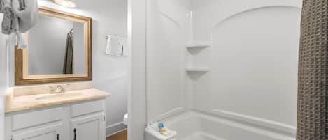 A bathroom with a white vanity, a large mirror, a bathtub, and a shower area.
