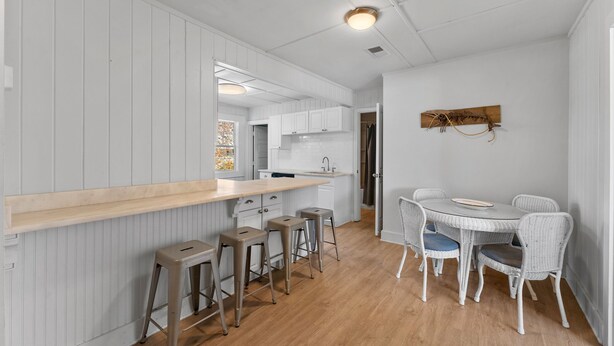Une cuisine moderne avec des meubles blancs, un plan de travail en bois et un coin repas doté de chaises en osier.