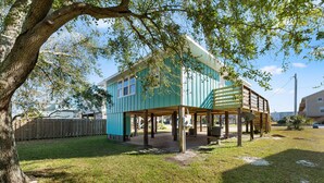 Une maison à deux étages avec une terrasse couverte et un grand arbre au premier plan.