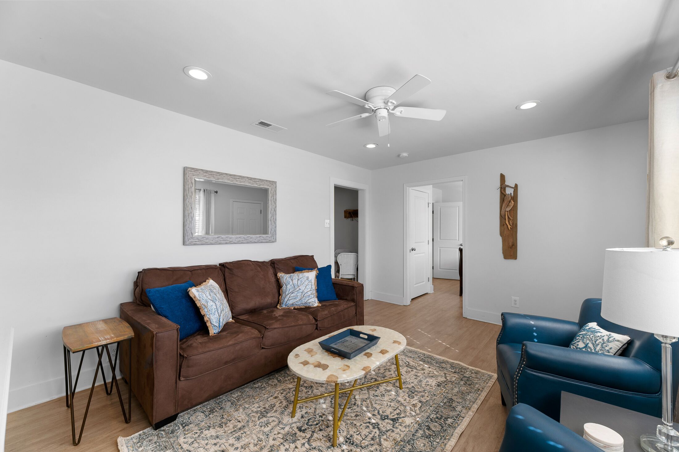 A living room with a brown leather sofa, a blue armchair, a small coffee table, and a ceiling fan.
