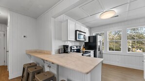 Une cuisine avec des meubles blancs, un grand îlot central doté de tabourets, un four à micro-ondes, une machine à café et un réfrigérateur.