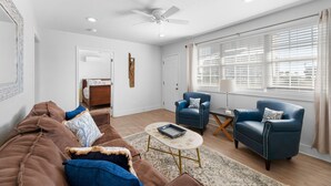 Un salon avec un canapé marron, deux fauteuils bleus, une table basse et un ventilateur de plafond.