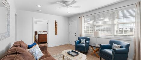 A living room with a brown sofa, two blue armchairs, a coffee table, and a ceiling fan.