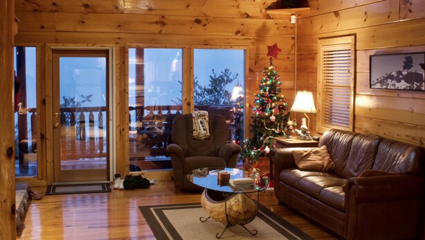Un interior acogedor de cabaña con detalles de madera, un sofá de cuero, una mesa de centro de cristal y un árbol de Navidad.