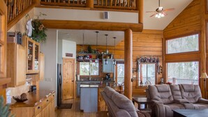A spacious cabin interior with a wooden dining area, a kitchen with a central island, and a cozy seating area with a sofa and chairs. - Stunning Log Cabin w/ Hot Tub, 3 Kings+ 4 BRms & loft - 2 flat screen TV's (Garden Valley)