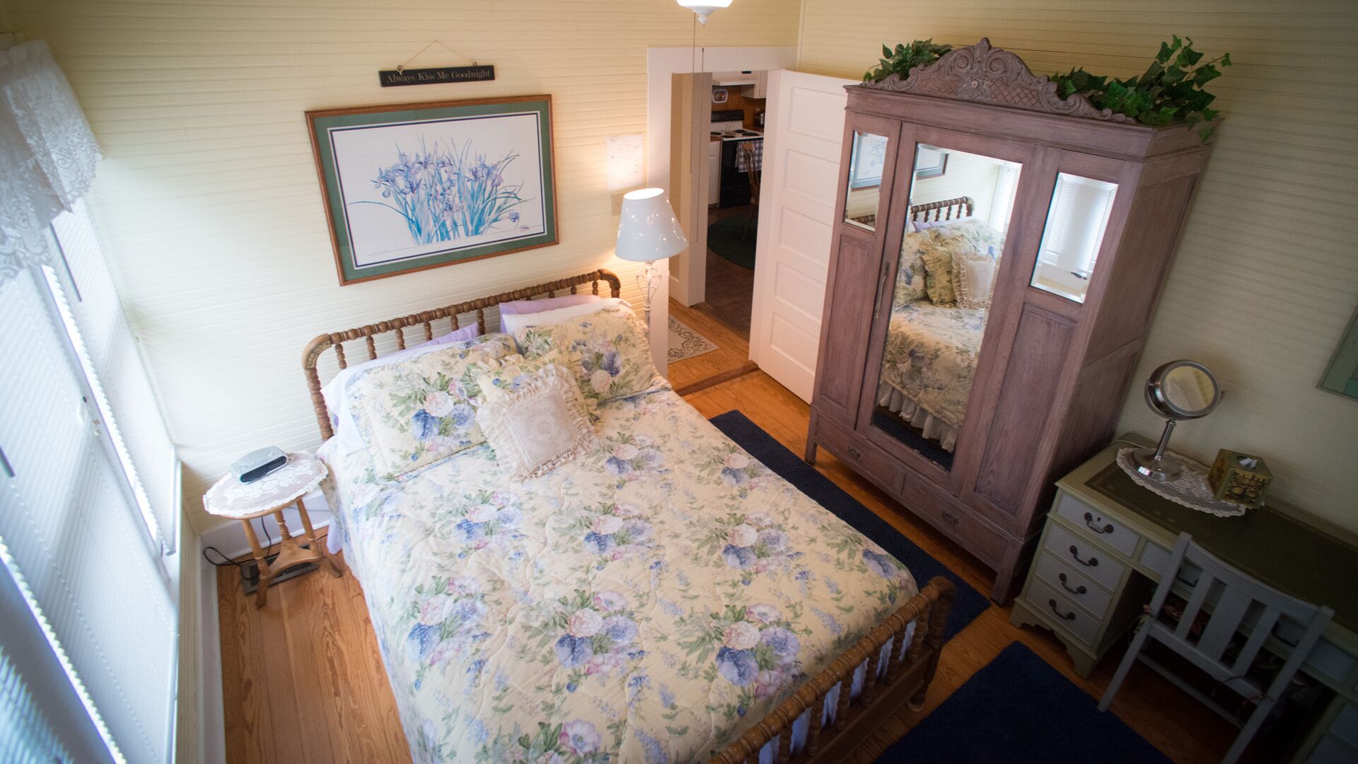 A bedroom with a floral bedspread, a bedside table, a wardrobe, and a mirror.