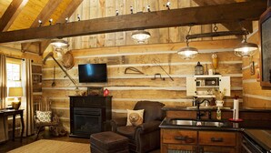 A rustic cabin interior with a fireplace, leather armchair, wooden walls, and a kitchen area.