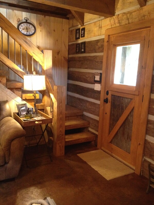 A wooden interior with a staircase, a clock, and a door with a window.