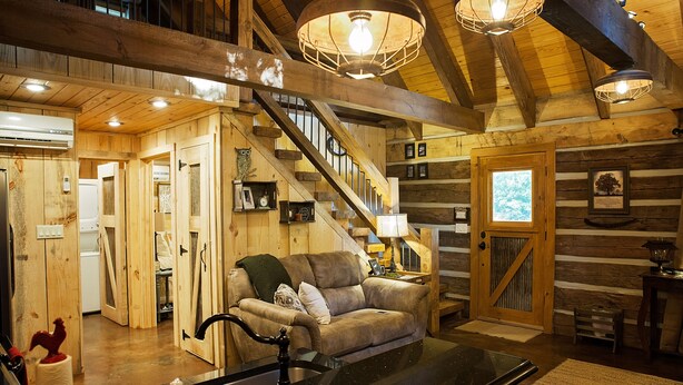 A log cabin interior with a staircase, a living room with a sofa, and a kitchen area.