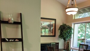 Un coin repas comprenant une table à plateau en verre, des chaises en bois, un buffet en bois foncé et un luminaire suspendu.