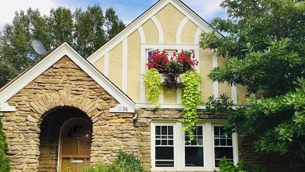 A stone building with a pitched roof, a window with hanging flower baskets, and a door with a bear statue. - 
Luxe  Fully Furnished 5 Star Home in Hyde Park/ Cincinnati (Cincinnati)