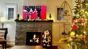 A living room with a fireplace, a television mounted above it, a Christmas tree, and a plush Santa Claus figure. - 
Luxe  Fully Furnished 5 Star Home in Hyde Park/ Cincinnati (Cincinnati)