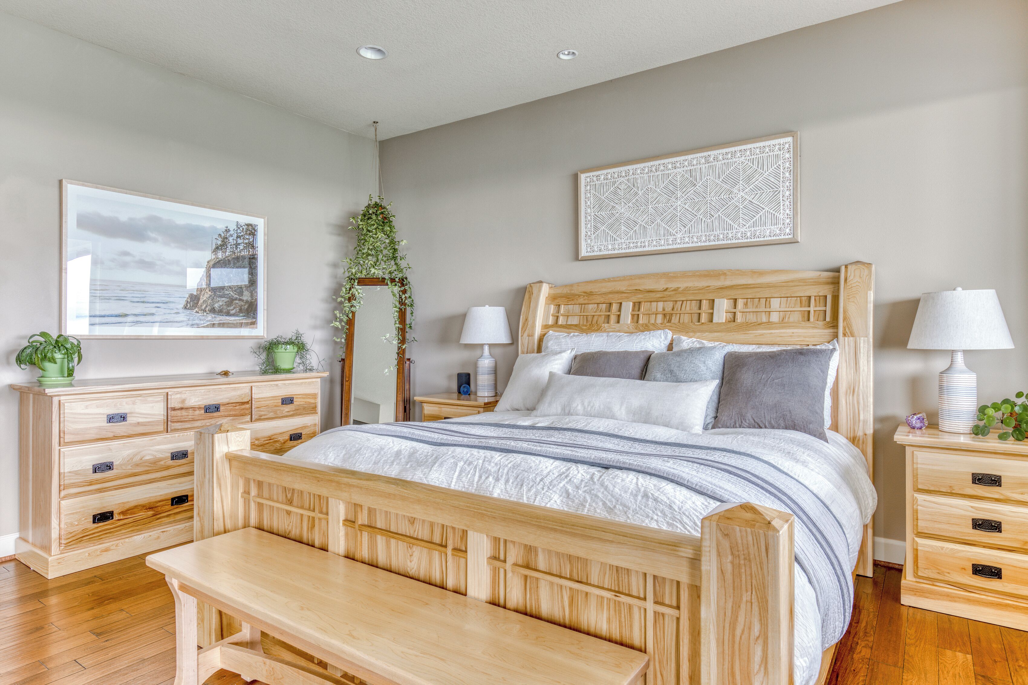 A bedroom with a wooden bed, bedside tables, a bench, a dresser, and a hanging plant.