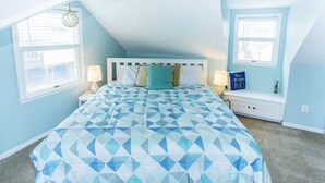 A bedroom with a sloped ceiling, a bed with a geometric patterned bedspread, two bedside tables with lamps, and a window with a view.