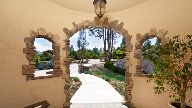 A stone archway leading to a garden with a pathway, a bench, and a potted plant.