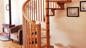 Uma escada espiral de madeira num quarto com um sofá, um aquecedor e quadros nas paredes.