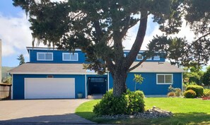 A two-story house with a garage, a large tree in front, and a well-maintained lawn. - Riverside Beach House (Seaside)