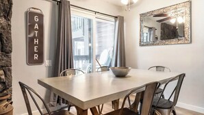 Ein Essbereich mit großem Tisch, Stühlen, einer Schüssel, einem Deckenventilator, einem Fenster mit Vorhängen und einem wandmontierten Spiegel.