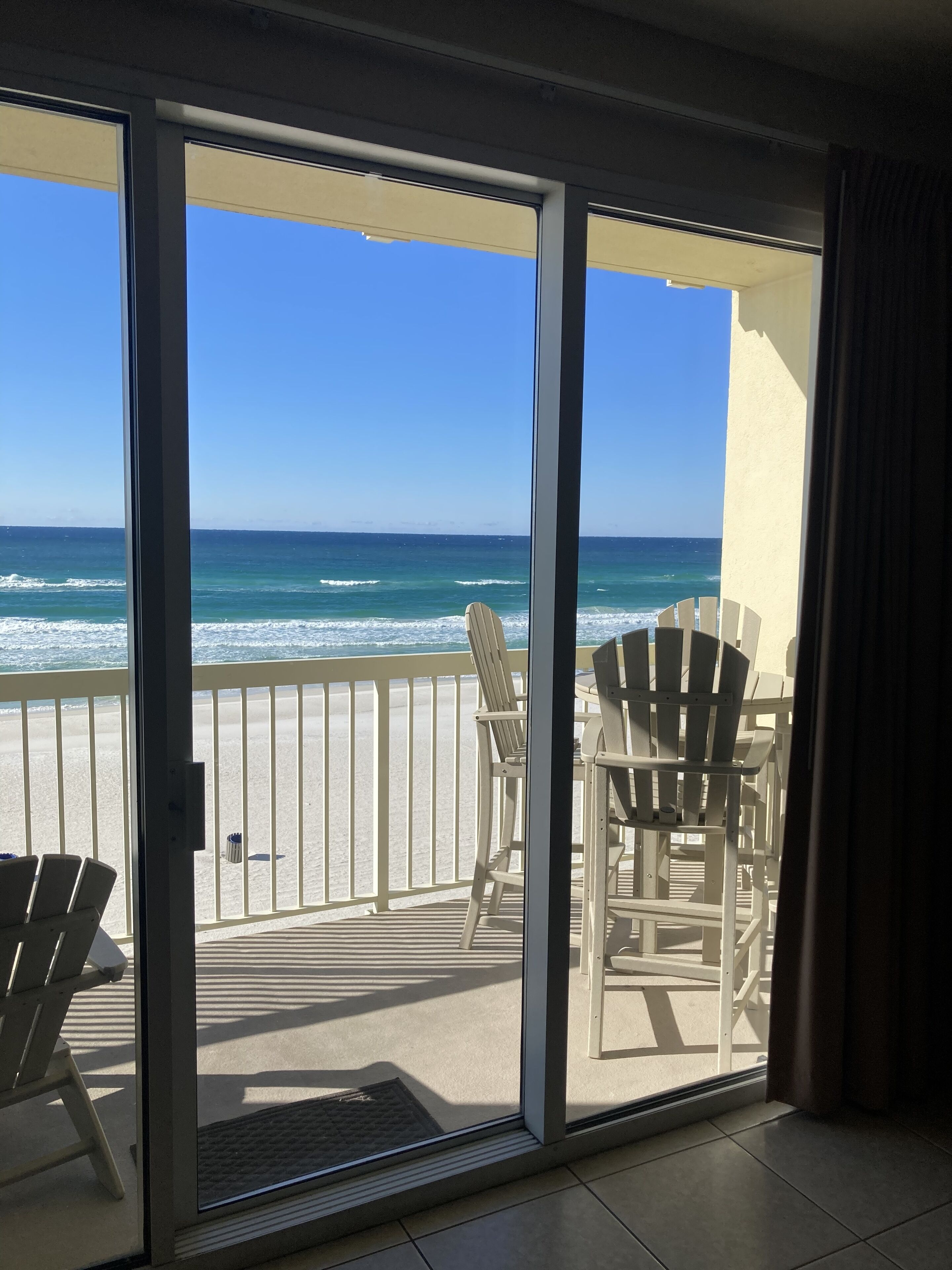 A balcony with a view of the ocean, featuring two Adirondack chairs and a small table.