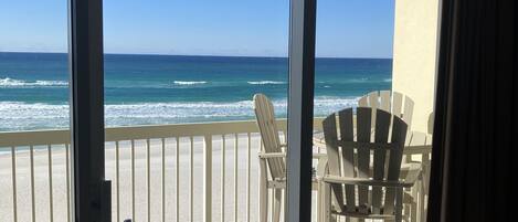 A balcony with a view of the ocean, featuring two Adirondack chairs and a small table.