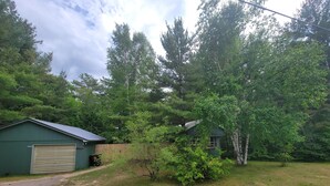 Ett grönt hus med ett garage, omgivet av träd och en gräsklädd trädgård.