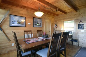 A wooden cabin interior with a dining table, chairs, framed pictures, and a hanging light fixture. - Purple Haze: Log Cabin, near Blue Ridge Pky, spectacular views and hot tub (Boone)