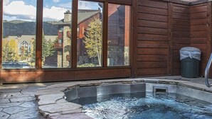 Un jacuzzi con escalones de piedra, paredes de madera y vistas a edificios y árboles.