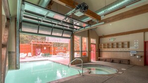 Piscina interior con cerramiento de vidrio, zona de sauna y área de asientos con bancos.