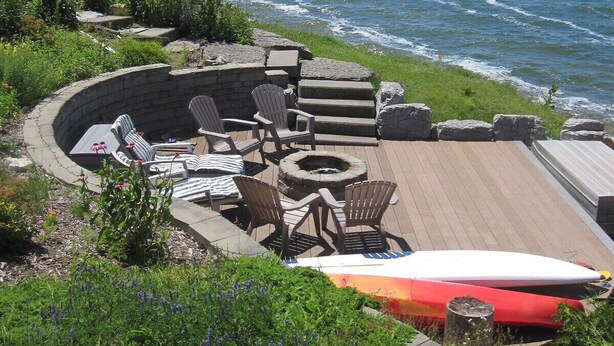 Een terras aan het water met buitenmeubels en een vuurkorf.