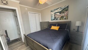 Ein Schlafzimmer mit Bett, Nachttisch, Lampe, einem Gemälde, Deckenventilator und einer Tür.