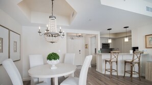 Una cocina moderna con armarios blancos, una isla central con taburetes y una lámpara de araña.