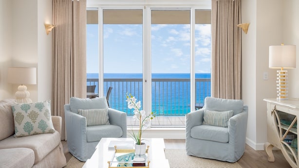 Un salón con dos sillones azul claro, una mesa de centro blanca con un jarrón de flores y vistas al océano a través de amplias puertas correderas.