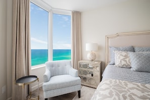 A bedroom with a large window, a chair, a bedside table with a lamp, and a bed with patterned bedding. - FALL BOOKINGS NOW! (Destin, Florida)