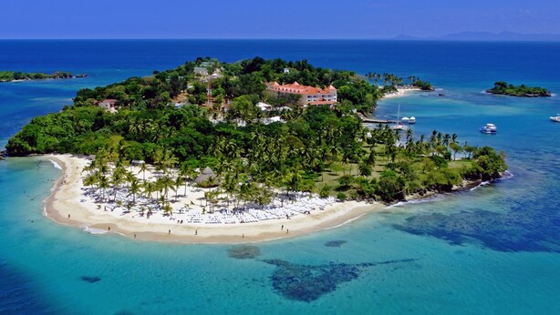 Une vue aérienne d’une île tropicale avec une plage, des palmiers et quelques bâtiments.