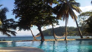 Une piscine avec un hamac et des palmiers, entourée d’une plage et offrant une vue sur l’océan.