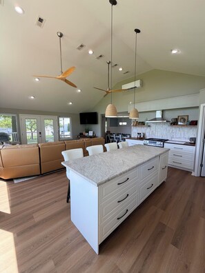 Un'ampia cucina con isola centrale, luci a sospensione, ventilatori a soffitto e un design moderno.