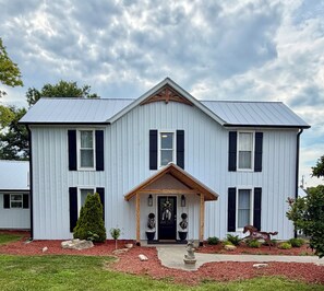 A two-story house with a symmetrical facade, a central entrance with a porch, and a small garden area with mulch and plants. - Glenn Acres Farm, Fishing and Relaxing, a Place Everyone Loves! (Columbia)