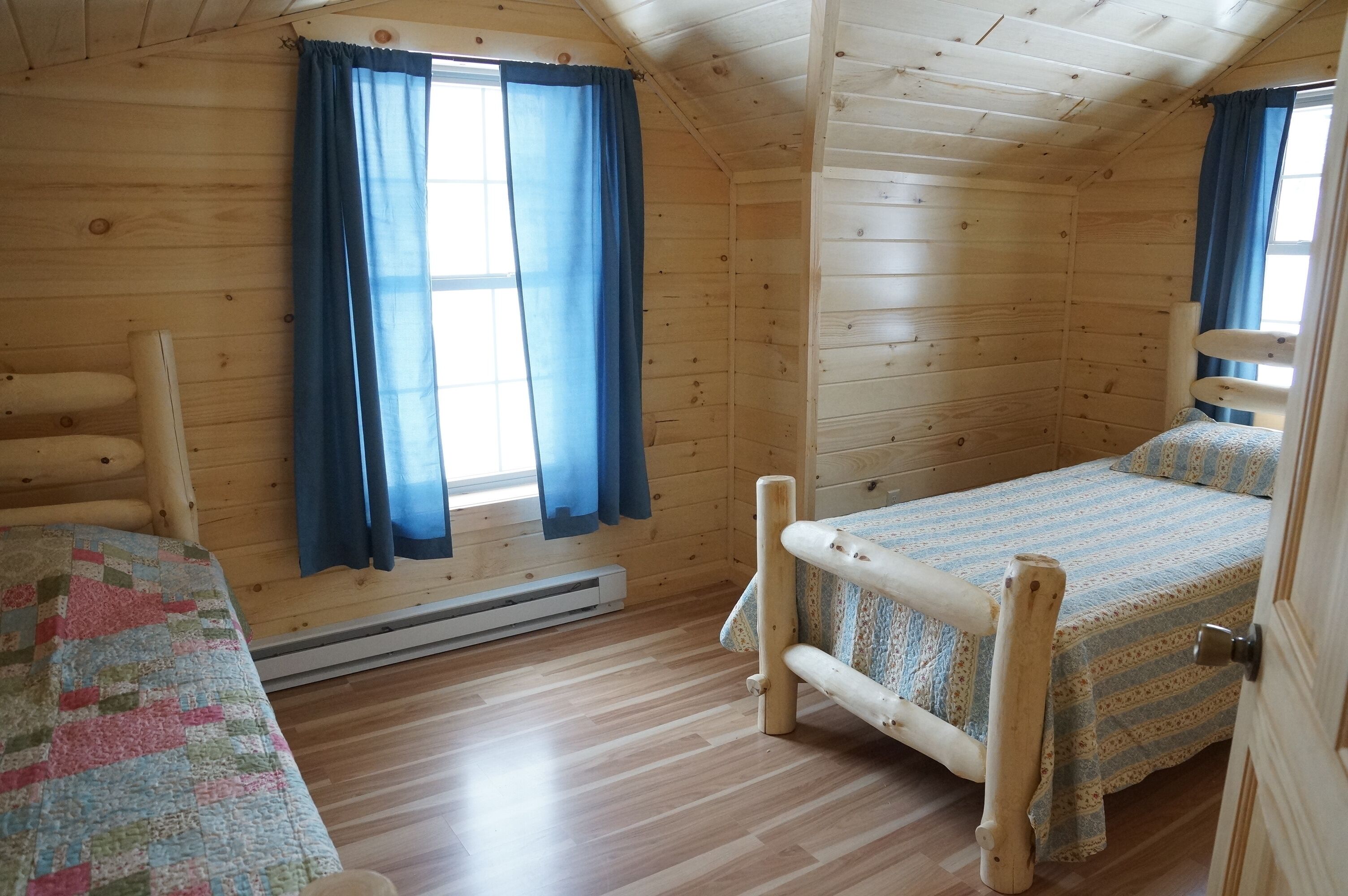 Una habitación de cabaña de madera con una cama, una mesita pequeña y una ventana con cortinas.