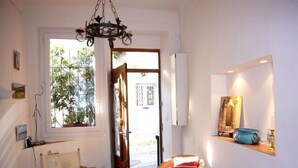 A room with a wooden chair, a small table, a book, a mirror, and a window with a view of greenery outside. - Charming Village House In Medieval Village, Close To Beach And Nice (Cagnes-Sur-Mer)