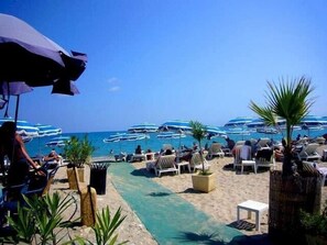 A beachside resort with lounge chairs and umbrellas, a clear pool, and boats in the background. - Charming Village House In Medieval Village, Close To Beach And Nice (Cagnes-Sur-Mer)