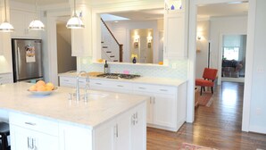 A modern kitchen with white cabinetry, a stainless steel refrigerator, and a large island with a sink. - Modern Farmhouse in Historic Downtown Bozeman (Bozeman)