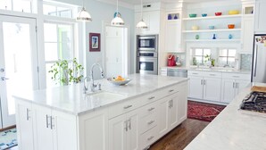 A modern kitchen with white cabinetry, a large island with a sink, an oven, and a stove. There are pendant lights above the island, and a red rug on the floor. - Modern Farmhouse in Historic Downtown Bozeman (Bozeman)