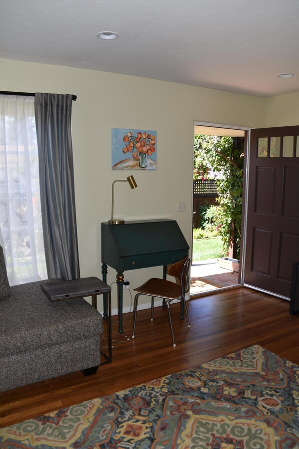 Una habitación con un escritorio verde, un sofá gris, un tapete estampado y una puerta que da a un jardín.